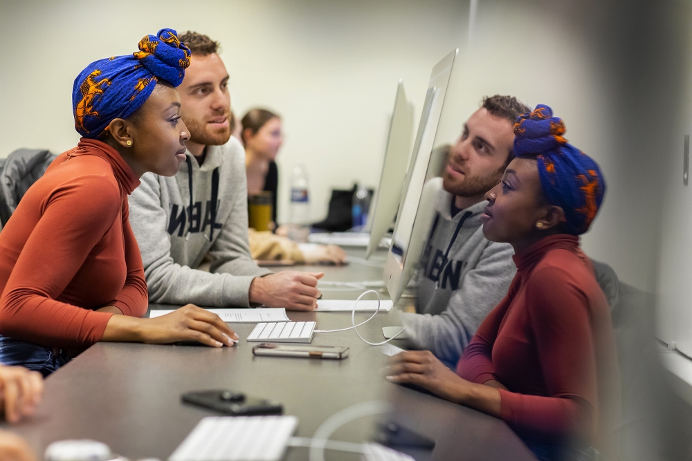 Two students working at a computer with their reflections shown at the right.