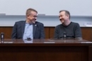 Representatives Bryan Cutler and Peter Schweyer sit at a table in front of a white board and face each other, laughing.