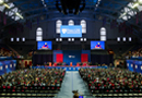 Penn GSE University of Pennsylvania, with graduates seated in the Palestra under banners, facing a stage where a Angela Duckworth is visible on two large screens.