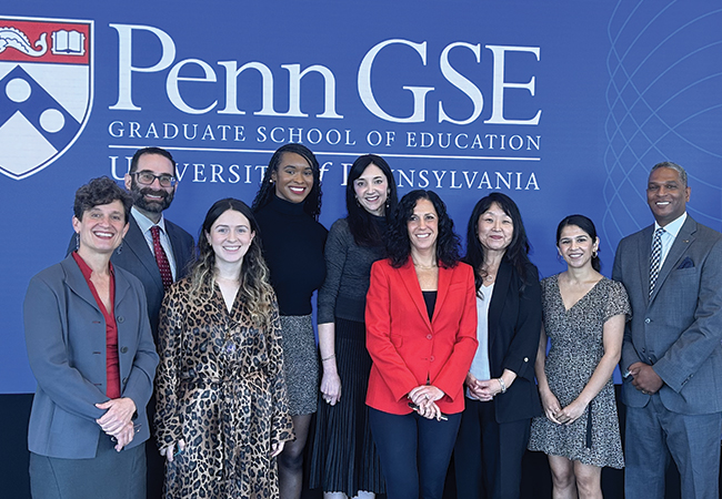 EdEnt Founding Director Jenny Zapf (far left), Penn GSE Dean Katharine Strunk (fourth from right), Associate Dean Susan Yoon (third from right), and six EdEnt program alum from five different cohorts pose in business casual attire in front of a blue Penn GSE banner