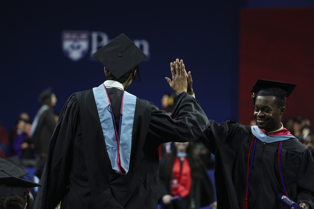Two students in their cap and gowns high five each other holding their diplomas