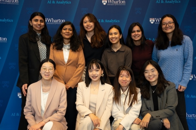 10 Penn students pose for a photo, four seated and six standing behind them, in front of a Wharton AI + Analytics background