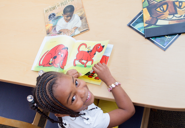A girl looks up from reading a picture book. 