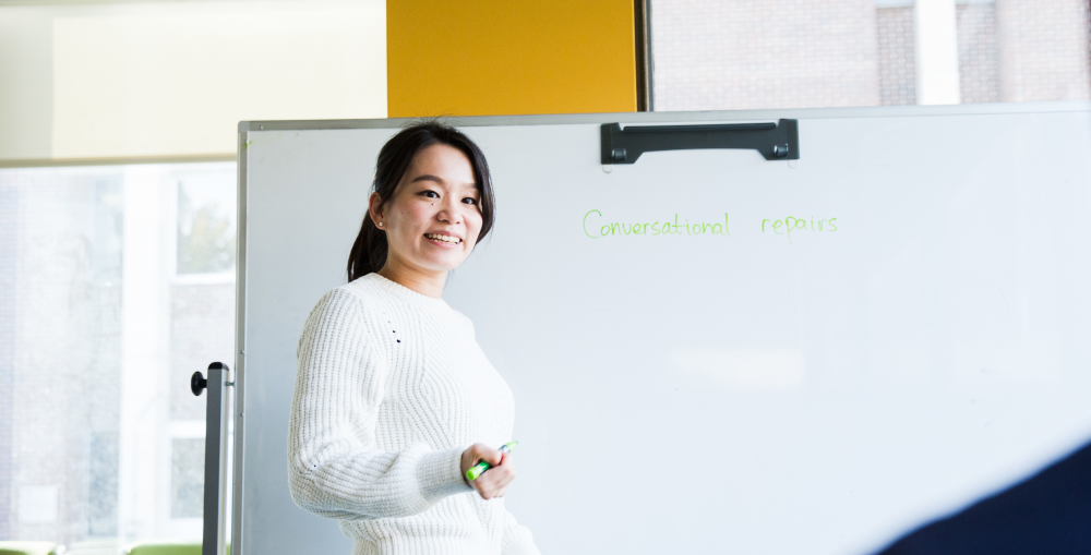 Student wearing white standing in front of a whiteboard.