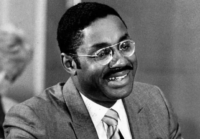 Black-and-white historical photo from the 1960s of Marcus Foster wearing a suit and tie and glasses. 