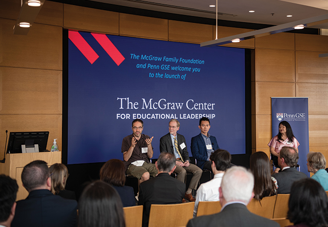 Three panelists and a moderator sit on stools in front of a seated audience in a wood-paneled lecture hall with a screen behind them reading "The McGraw Center for Educational Leadership"