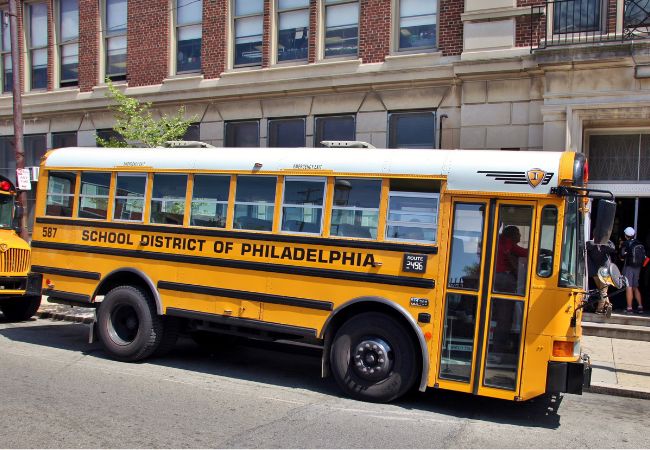 A yellow School District of Philadelphia school bus parked in front of a school.