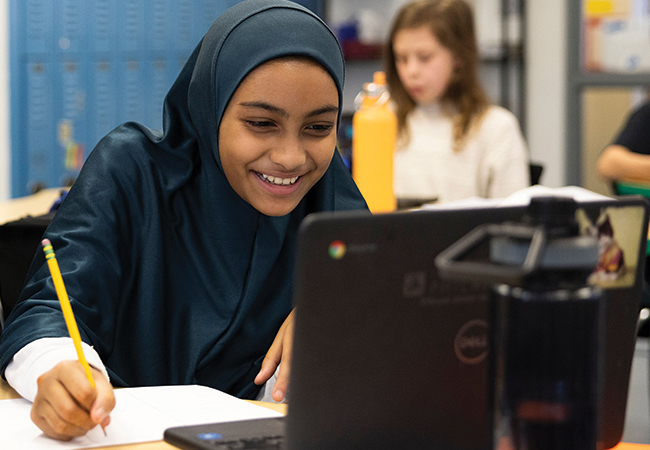 A smiling student at Penn Alexander elementary school does work on a computer.