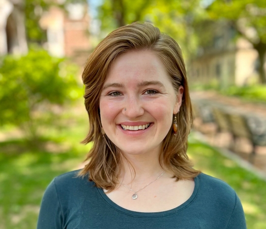 Headshot of Penelope Lusk smiling against green nature and stone building