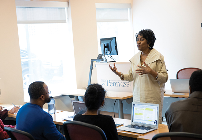 Professor Gadsden addresses graduate students who are listening intently with laptops or notepads open in front of them, in a bright classroom.