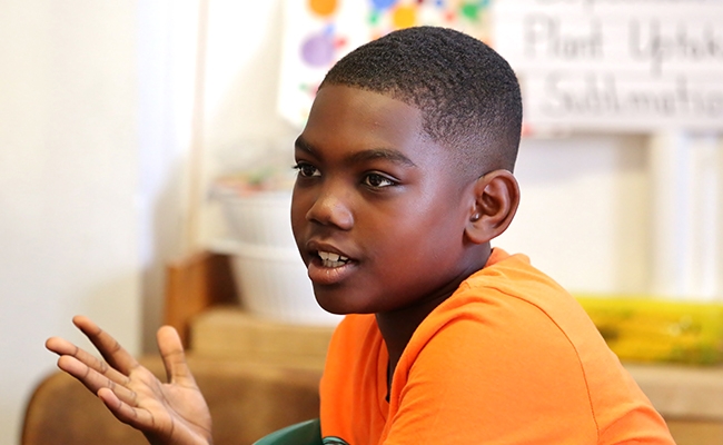 Young boy in orange shirt sitting and talking in classroom
