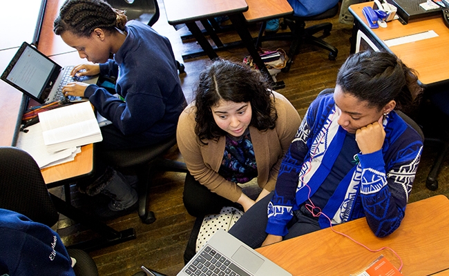 Aerial view of teacher kneeling next to student on laptop