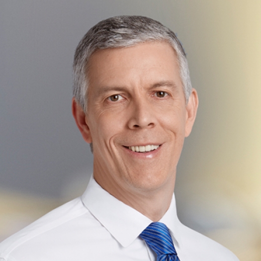 A headshot of Arne Duncan in a white button-down shirt and blue tie