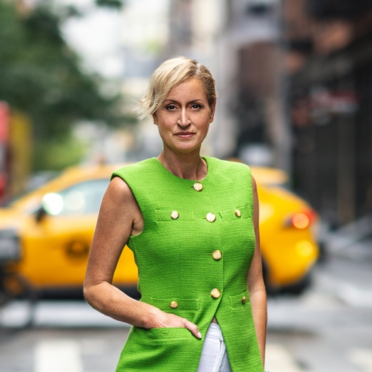 Kandi stands in a New York City street in a bright green top in front of a yellow taxi.