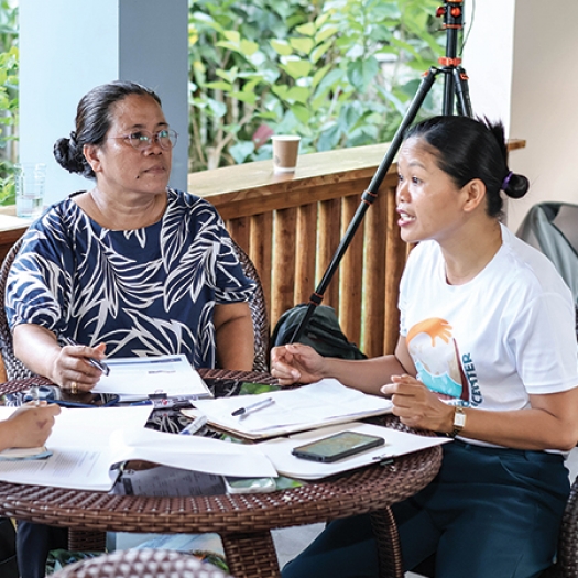 Three women sit around a table with pens and paper having a discussion