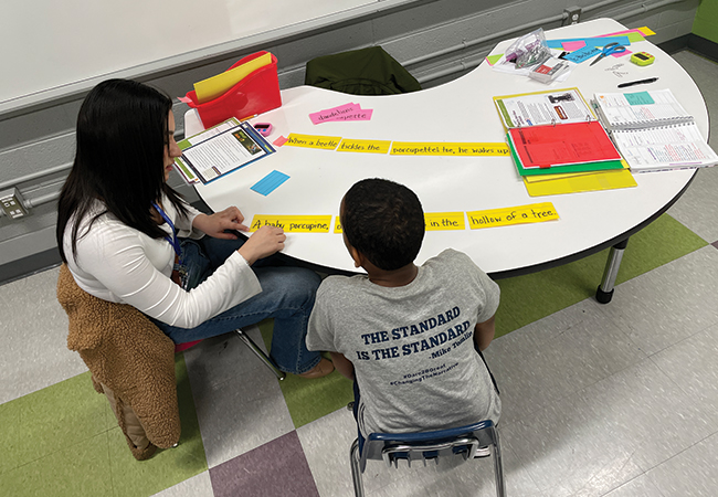 Penn Arts & Sciences undergrad Sarah Alvarado tutors a Hamilton Elementary student in reading at a small table in a classroom