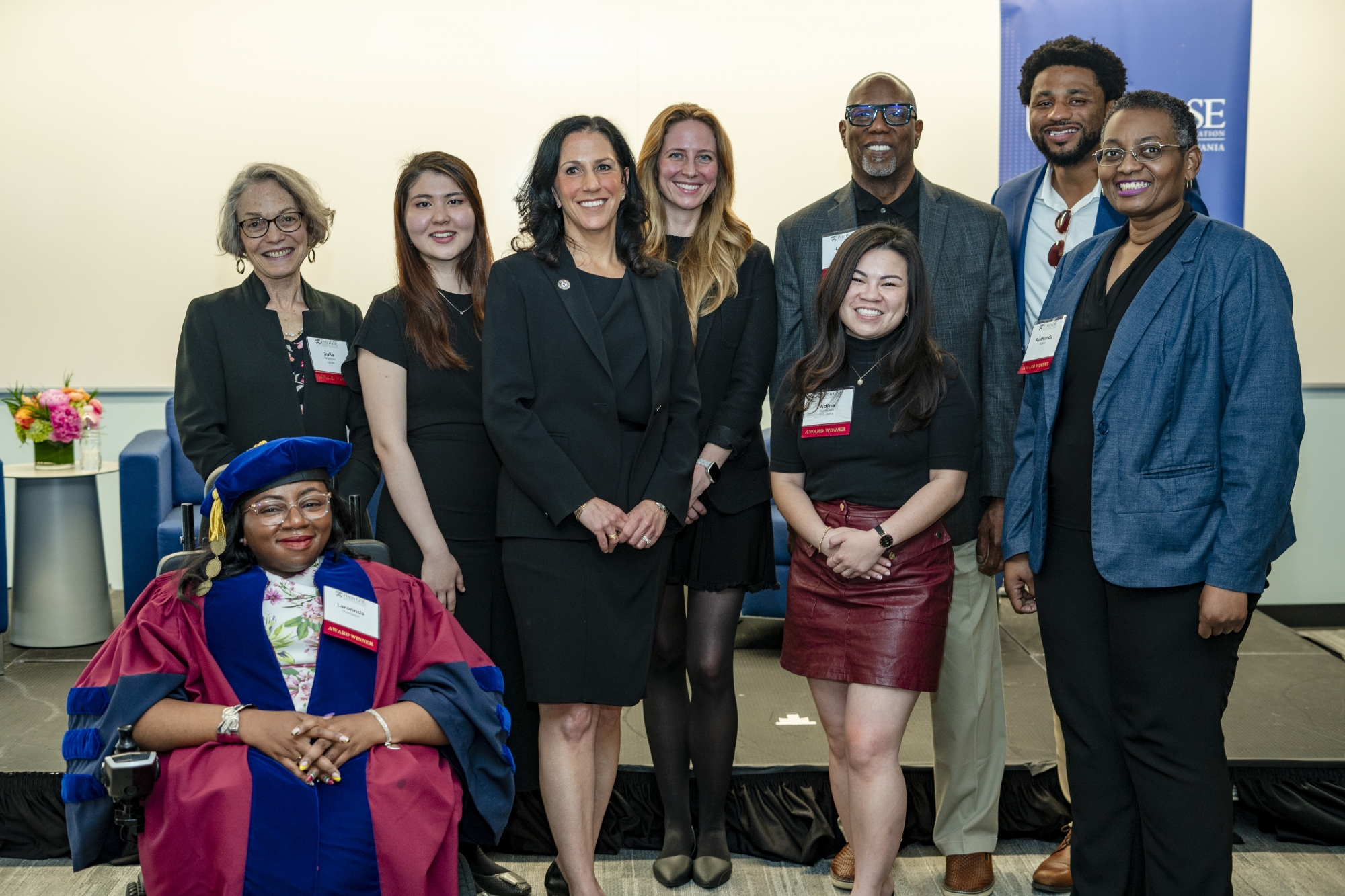 Nine award winners, including one in her red-and-blue graduation tam and gown, pose onstage with the dean after the 2024 Celebration of Educators event.