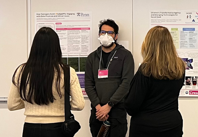 A man stands in front of a poster on the wall describing his research to two conference attendees.